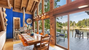 Cozinha moderna com mesa e cadeiras de madeira, janelas amplas e vista para um deck e um lago.