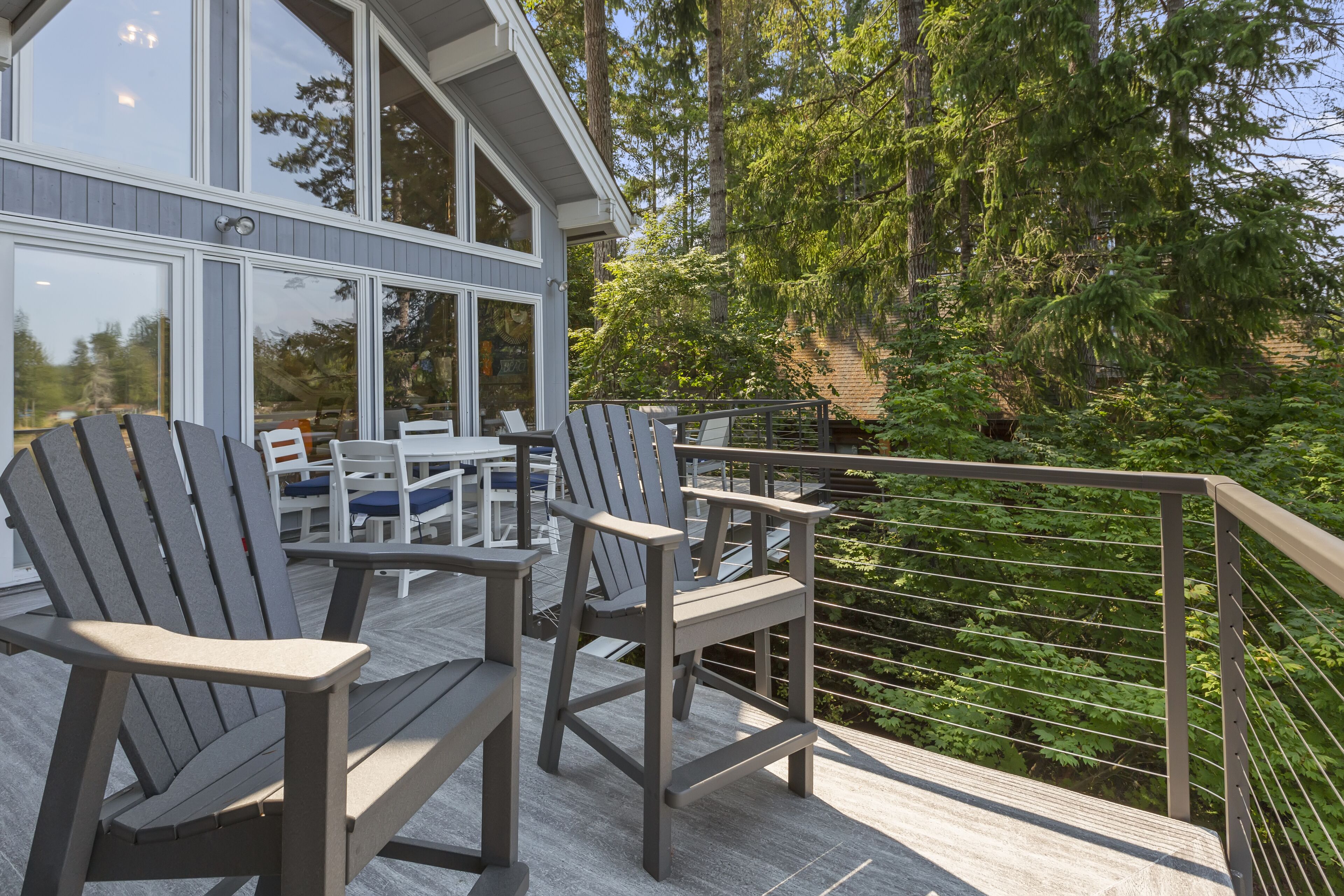 A deck with Adirondack chairs and a table, overlooking a forested area.