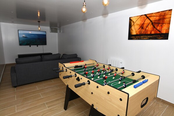 A modern living room with a foosball table, a large flat-screen TV, and a sofa. - The leaning house with private Jacuzzi (Rosny-sous-Bois)
