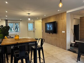 Un espace repas moderne avec une table en bois, des chaises noires et un téléviseur à écran plat fixé à un mur en bois.