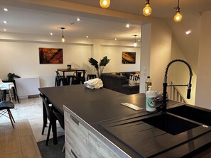 Une cuisine moderne avec un îlot central, un coin repas avec des chaises, un canapé et des œuvres d’art accrochées aux murs.
