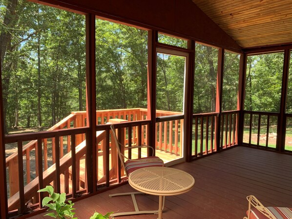 A covered outdoor deck with a wooden railing, a round table, and a bench.