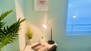 Une pièce avec un bureau, une plante en pot, un tableau encadré et une fenêtre donnant sur un paysage.
