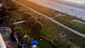 Une vue sur la plage au coucher du soleil, un espace piscine avec des chaises longues et un sentier menant à la plage.