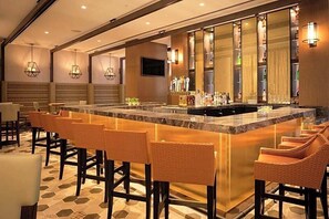 A bar area with a marble countertop, wicker bar stools, and a variety of bottles and glasses.