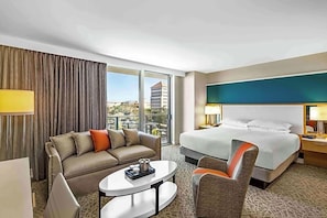 A hotel room with a large bed, a sofa, a small table, and a view of the city.