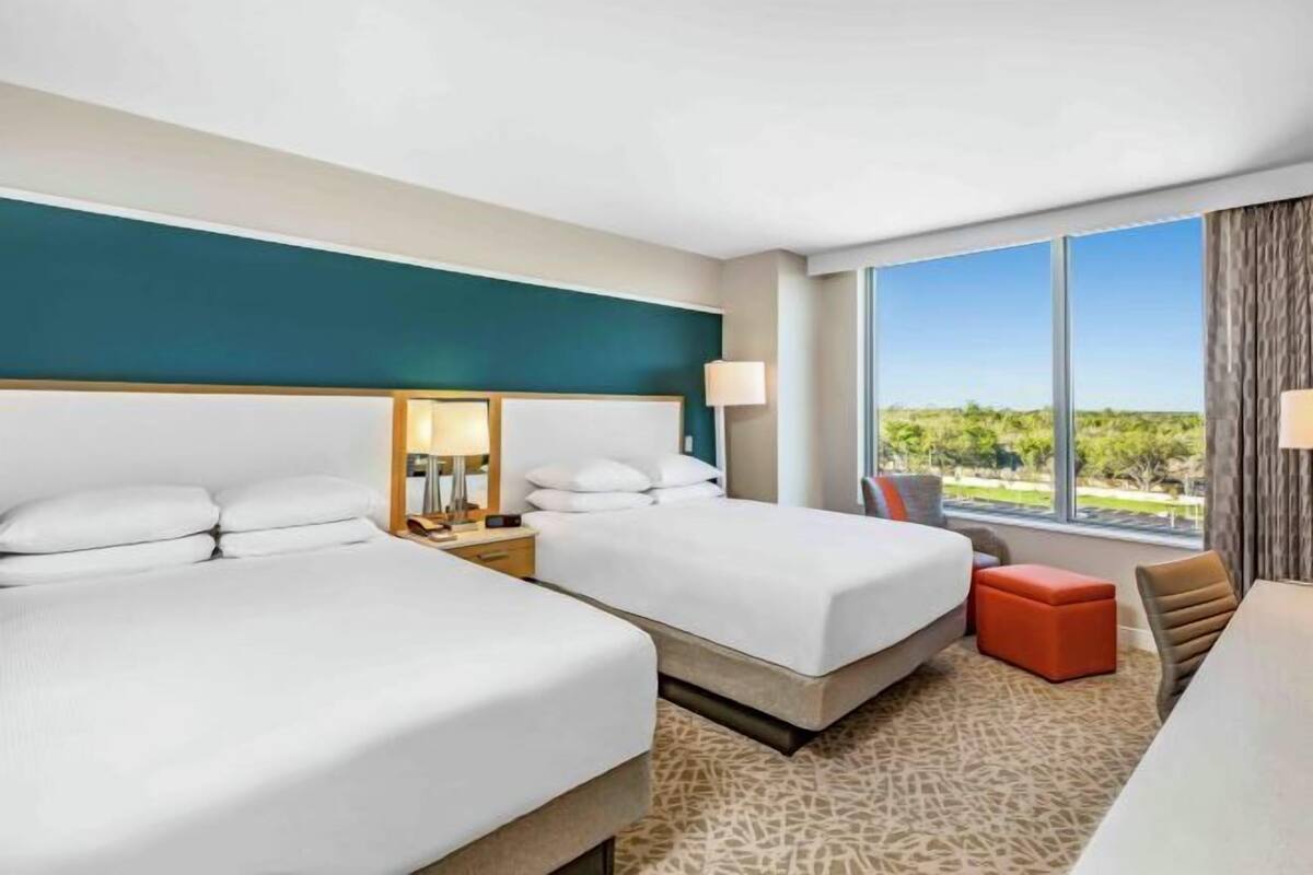 Ein Hotelzimmer mit zwei Betten, einem Schreibtisch, einem Stuhl und einem großen Fenster mit Blick.