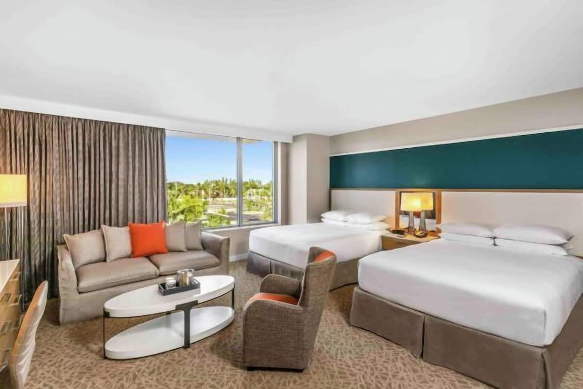Ein Hotelzimmer mit einem großen Bett, einer Couch, einem kleinen Tisch und Blick auf Grünfläche.