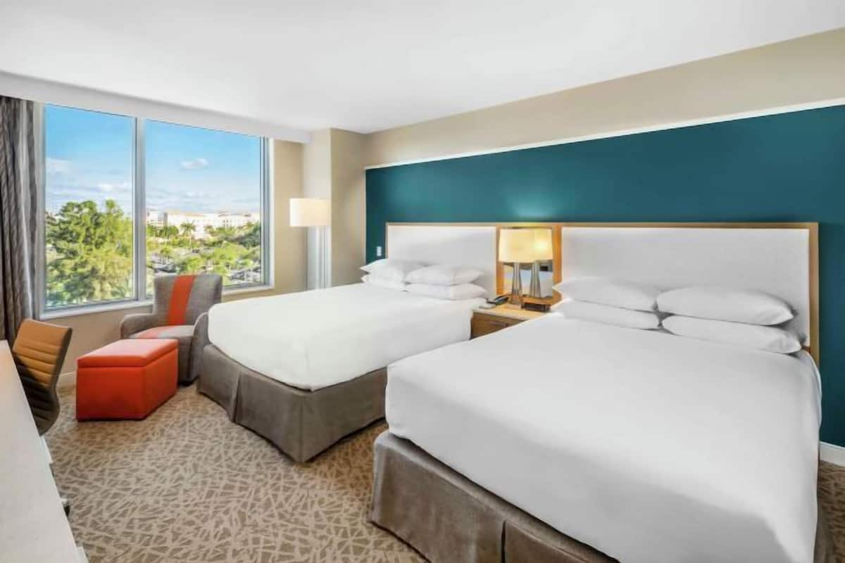 Ein Hotelzimmer mit zwei Betten, Blick auf die Stadt und einem großen Fenster.