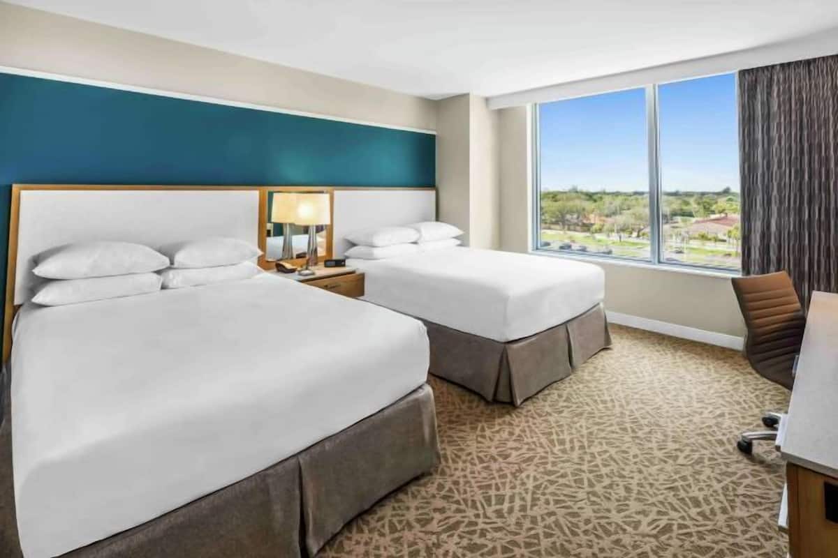 Ein Hotelzimmer mit zwei Betten, einem Schreibtisch und einem großen Fenster mit Blick.