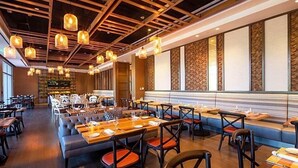 Un restaurant moderne avec des tables en bois, des sièges rembourrés et des luminaires suspendus.