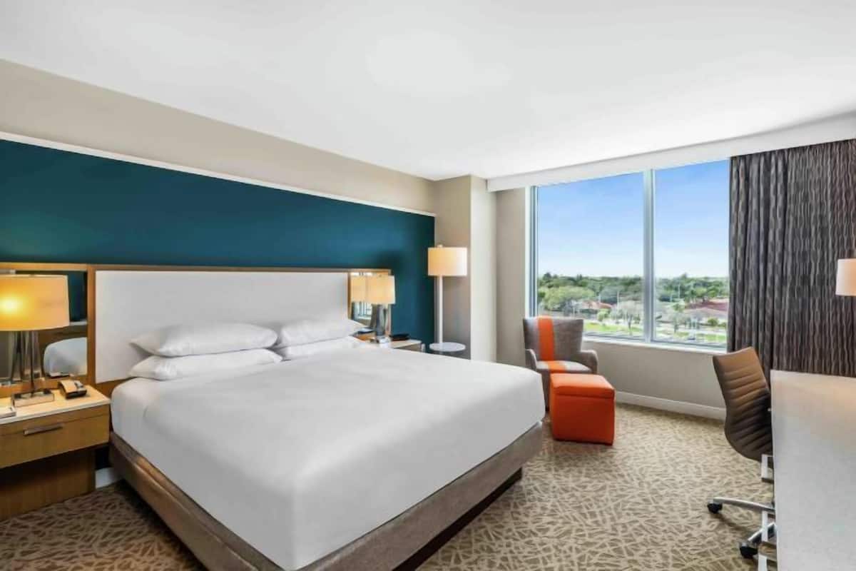 Ein Hotelzimmer mit einem großen Bett, einem Schreibtisch, einem Stuhl und Blick ins Freie.