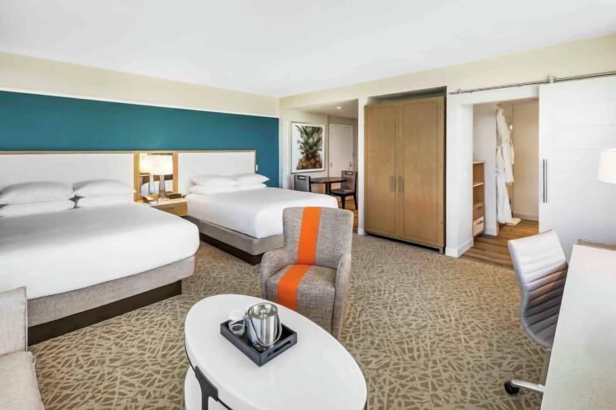 Ein Hotelzimmer mit zwei Betten, einem Esstisch, einem Stuhl, einem kleinen Tischchen mit Tablett und einem Kleiderschrank.