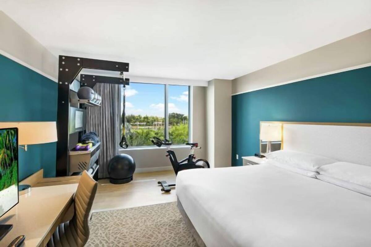 Ein Hotelzimmer mit Bett, Schreibtisch, Stuhl, Fitnessball und Fahrrad.