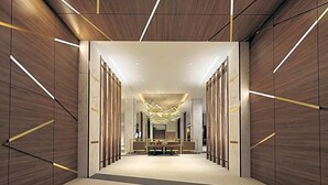 Un hall d’hôtel moderne doté d’un espace salon central, de lambris en bois et de luminaires aux formes géométriques.
