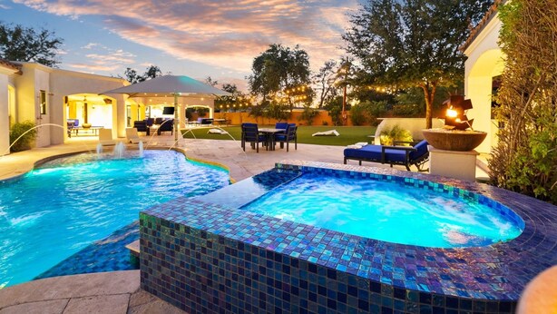 Une piscine avec un jacuzzi, entourée de chaises longues et d’un patio couvert.