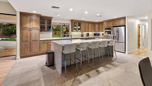 Une cuisine moderne avec des meubles en bois, un îlot central doté de tabourets de bar, des appareils en acier inoxydable et une vue sur l’espace extérieur.