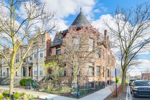 A historic building with a distinctive turret and brick facade, surrounded by trees and a sidewalk. - Victorian Mansion in Garfield Park (Chicago)
