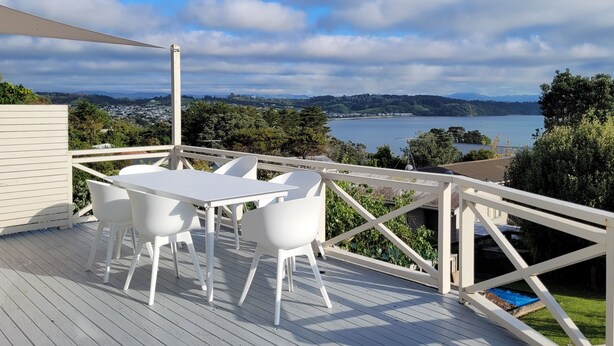 A deck with a table and chairs, overlooking a lake and distant hills. - Relaxing Spot with Stunning Sea View! (Snells Beach)
