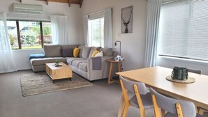 A modern living room with a sofa, coffee table, and dining table. - Relaxing Spot with Stunning Sea View! (Snells Beach)
