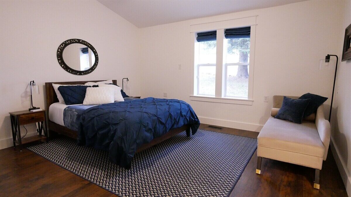 Une chambre à coucher avec un lit, des tables de chevet, une chaise, une fenêtre et un miroir.
