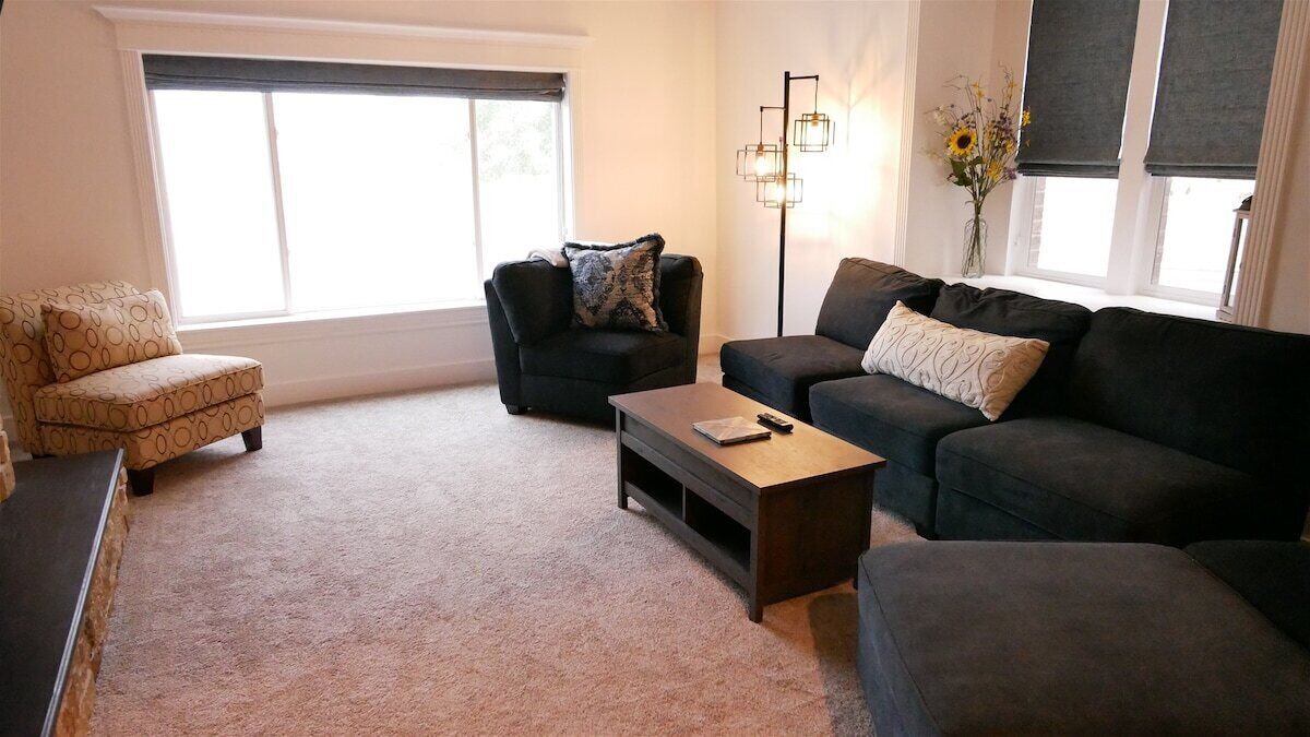 A living room with a sofa, armchair, and ottoman, a coffee table, and a floor lamp.