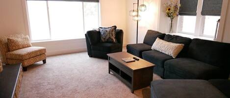 A living room with a sofa, armchair, and ottoman, a coffee table, and a floor lamp.
