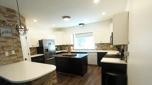 A modern kitchen with a central island, white cabinetry, a stone accent wall, and a hanging light fixture. - 6 Bed 6 bath Country Red Brick Home (Eden)