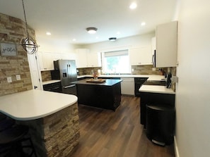 A modern kitchen with a central island, white cabinetry, a stone accent wall, and a hanging light fixture.
