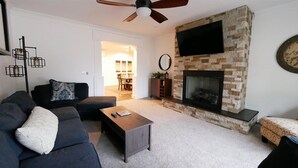 A living room with a fireplace, dark sofas, a coffee table, and a ceiling fan. - 6 Bed 6 bath Country Red Brick Home (Eden)