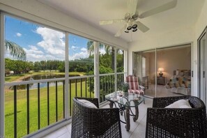 Ein Balkon mit Korbstühlen, einem Glastisch und Blick auf einen See und viel Grün.
