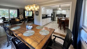 A spacious living room with a wooden dining table, a kitchen with white cabinets, and a dining area with a chandelier. - Updated in 2021 Notre Dame Football Weekend Entertaining Home (South Bend)