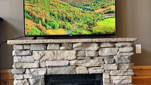Ein Fernseher über einem Kamin aus Stein, in dem ein Feuer brennt.