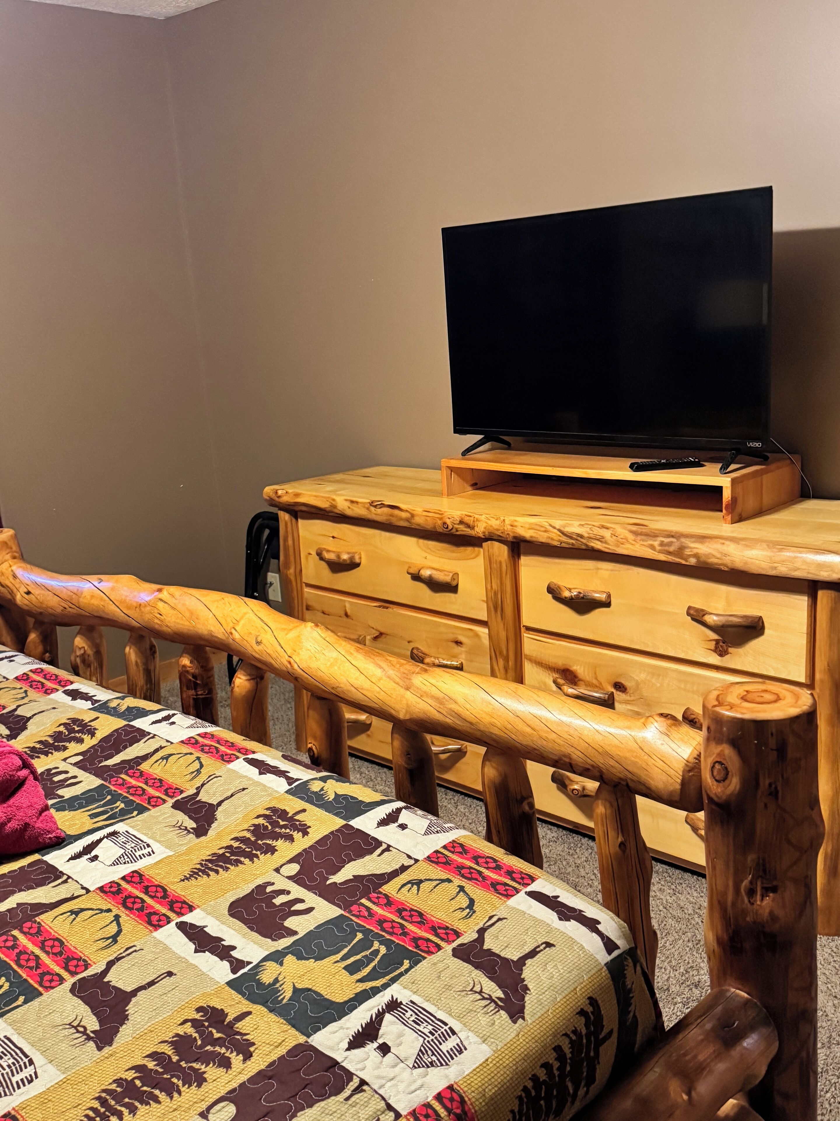 A room with a bed, a wooden dresser, and a television on a stand.