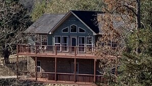 Eine zweistöckige Holzhütte mit Balkon, umgeben von Bäumen und einem Holzzaun.