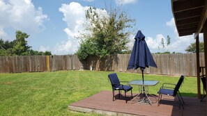Um espaço de pátio com mesa, duas cadeiras e um guarda-sol, além de um deck de madeira.