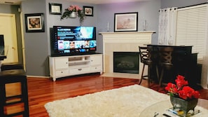 A living room with a flat-screen TV, white entertainment unit, fireplace, and a white shag rug.