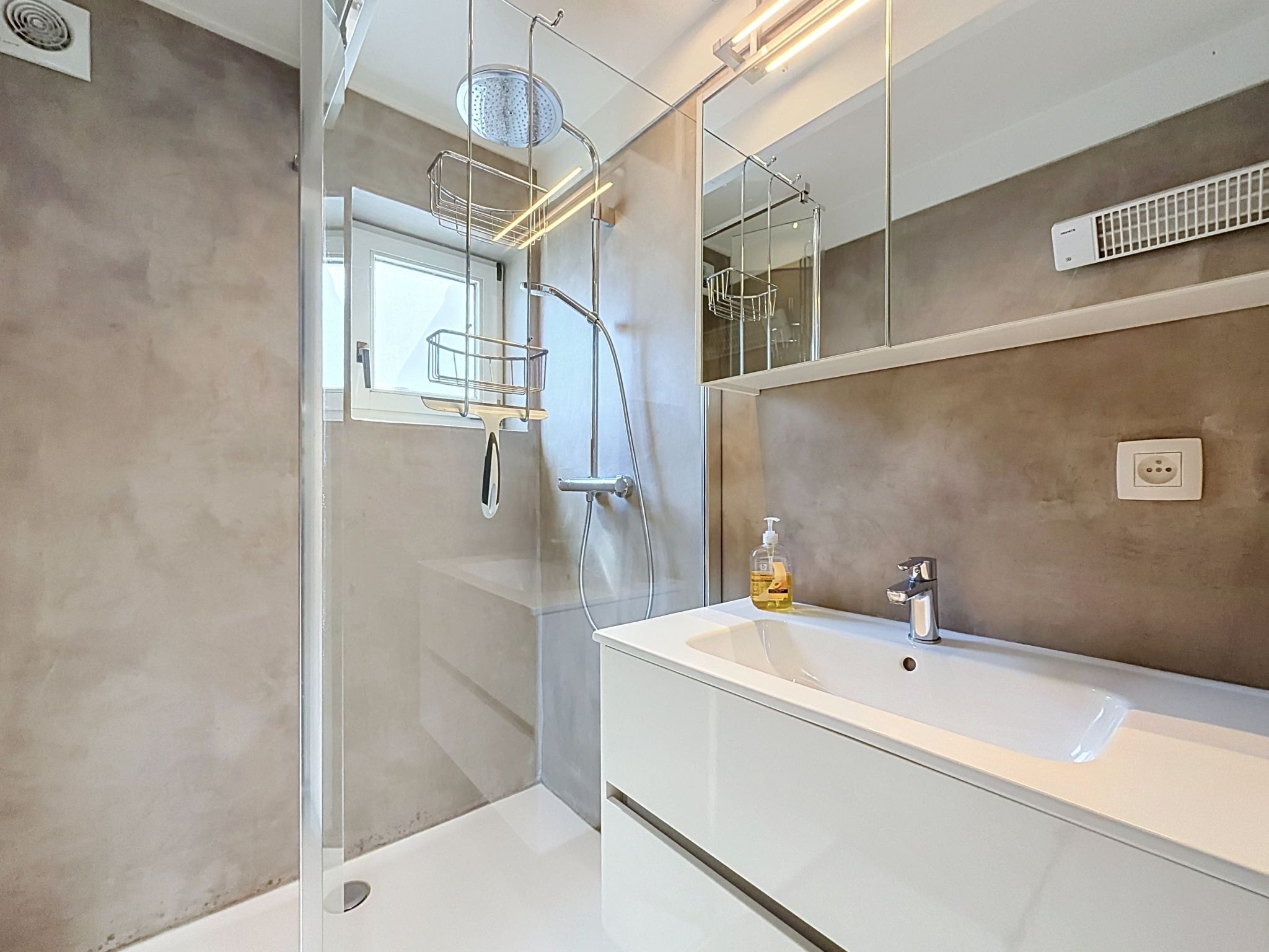 A modern bathroom with a glass-enclosed shower, a white sink, and a large mirror.