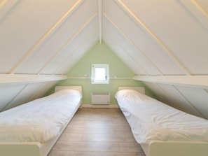 A small attic bedroom with two single beds, a window, and a radiator.