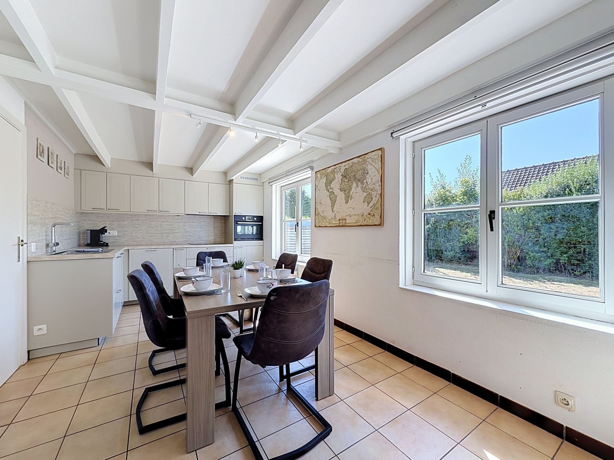 A modern kitchen with white cabinets, a dining table with chairs, and a large window with a view of greenery.