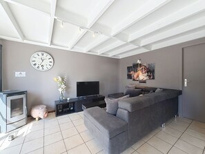 A modern living room with a grey sofa, a flat-screen TV, a fireplace, and a large wall clock.