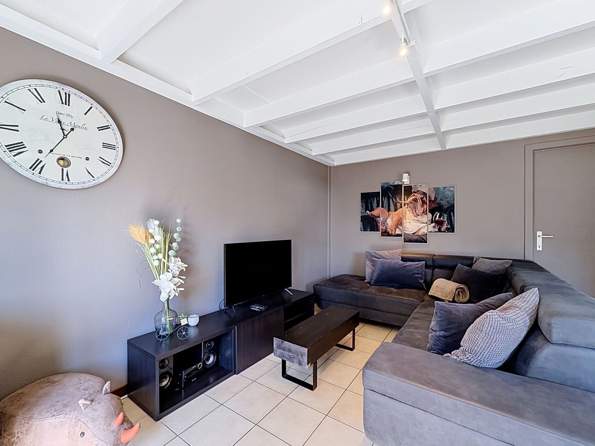A living room with a large wall clock, a flat-screen TV, a sofa, a coffee table, and a decorative sculpture.