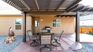 A covered patio with a table and chairs, a grill, and a decorative stone arrangement.