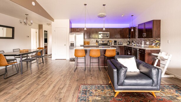 A modern kitchen with a central island, bar stools, and a dining area with a table and chairs.