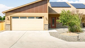 A modern house with a beige garage, a red door, and solar panels on the roof.