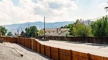 A road with a wooden fence on one side and a residential area with houses and mountains in the background.