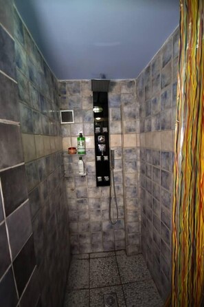 A small, tiled shower stall with a handheld showerhead and a shelf with toiletries. - Villa in Malaki in Sea With PlayGround (Malaki)