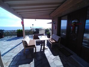 An outdoor patio with stone flooring, wooden furniture, and a view of the ocean. - Villa in Malaki in Sea With PlayGround (Malaki)