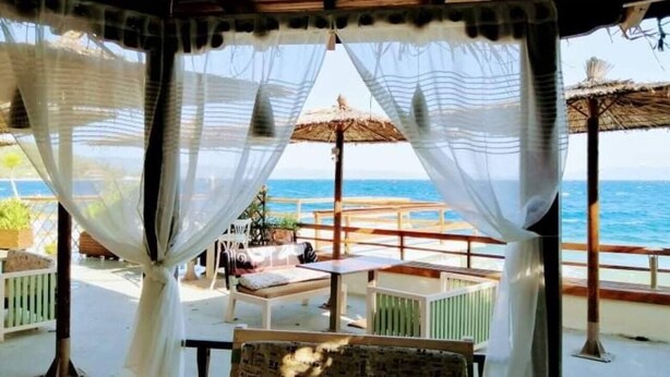A covered outdoor seating area with a view of the sea, featuring a table and chairs under a thatched roof. - Villa in Malaki in Sea With PlayGround (Malaki)