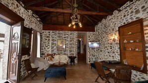 A rustic interior with stone walls, a wooden ceiling, a sofa, a dining table, and a television. - Villa in Malaki in Sea With PlayGround (Malaki)